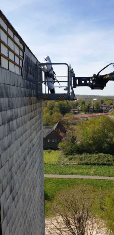 Vakman op hoogwerker bij asbestgevel hoog gebouw